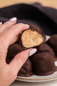 Hand holding one of the chocolate covered peanut butter balls and cut in half.