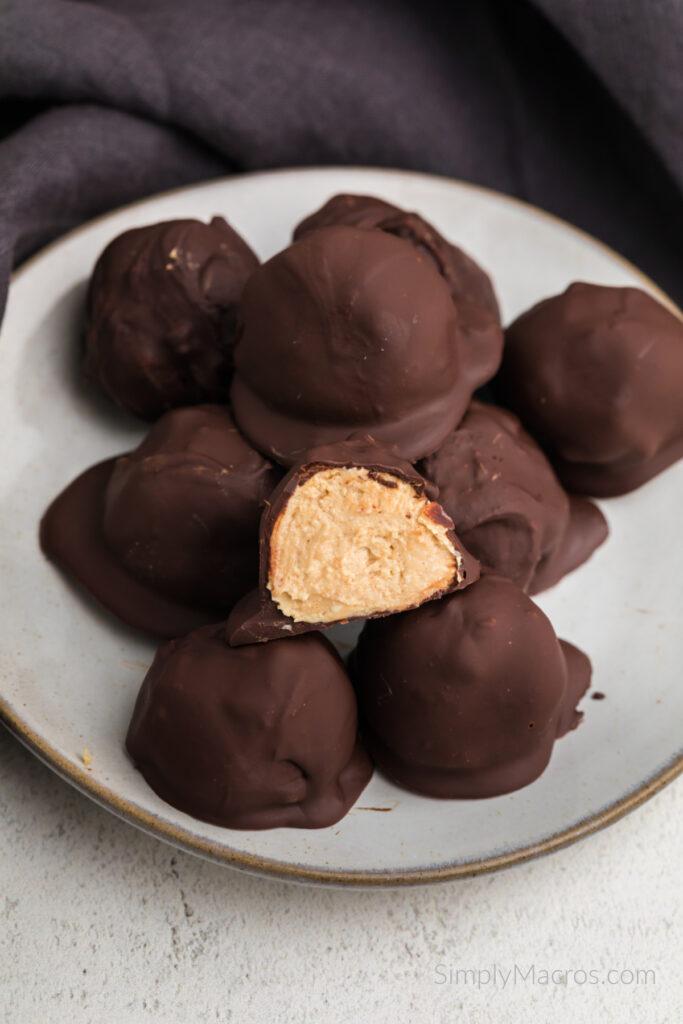 High protein peanut butter balls stacked on a plate, one cut in half. 