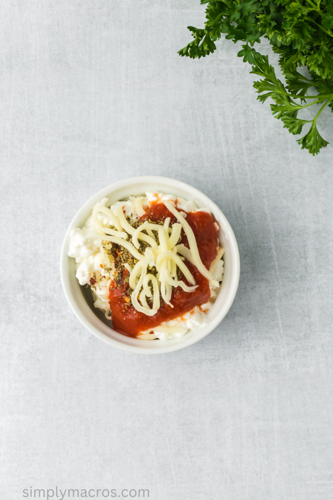 Cottage cheese, marinara, mozzarella, and seasonings added to a bowl. 