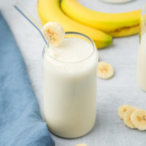 Banana Smoothie in a glass with a slice of banana on the rim. Ready to drink.