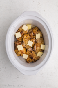 chicken thighs in a slow cooker with butter on top.