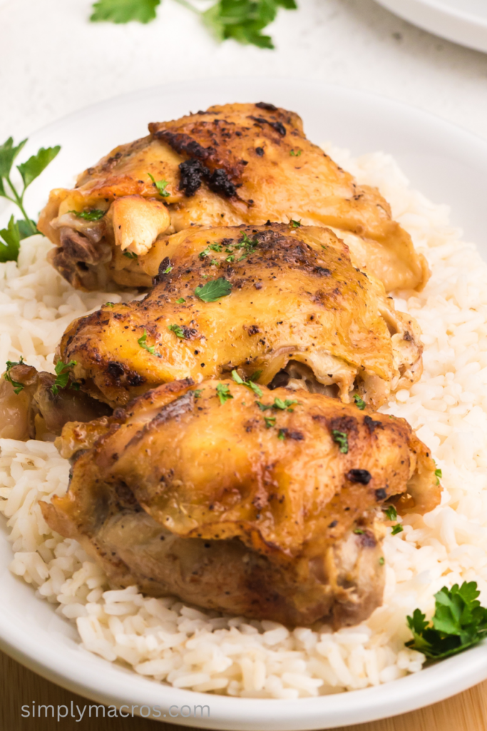 Close up of slow cooker chicken thighs served on a plate of rice. 