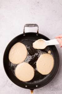 pancakes being poured into a skillet.