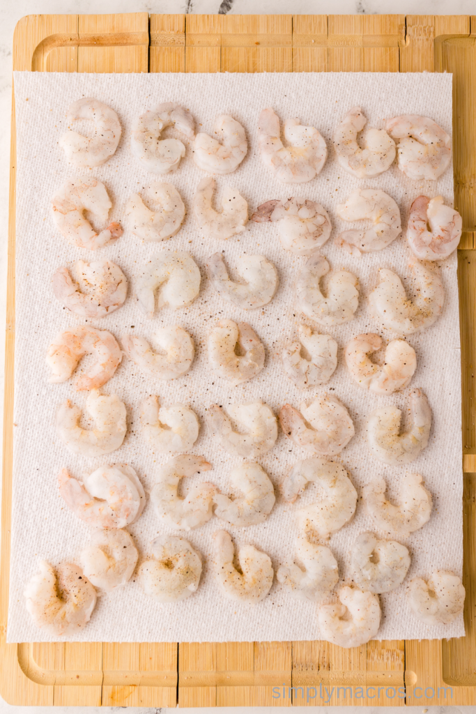Seasoned shrimp on a paper towel on top of a cutting board. 