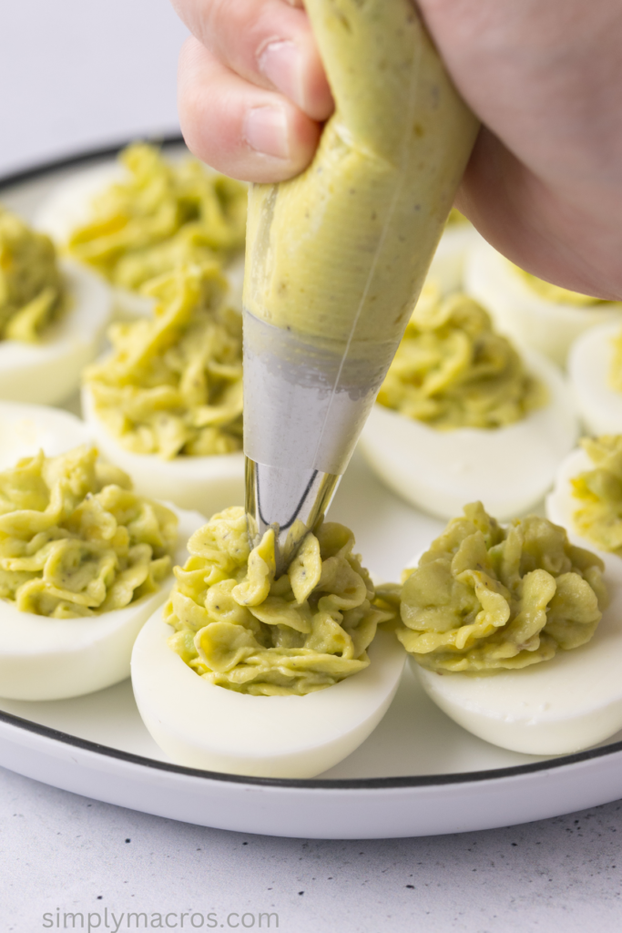Piping avocado egg mixture onto the egg whites to make the avocado deviled eggs.