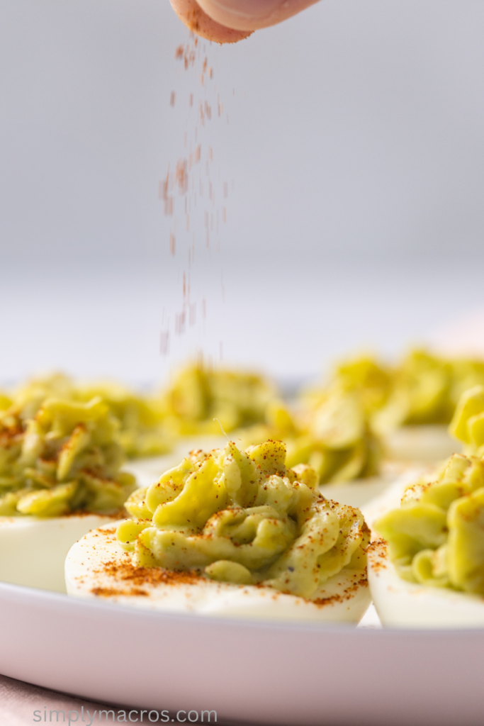 Adding paprika to the tops of the avocado deviled eggs before serving.