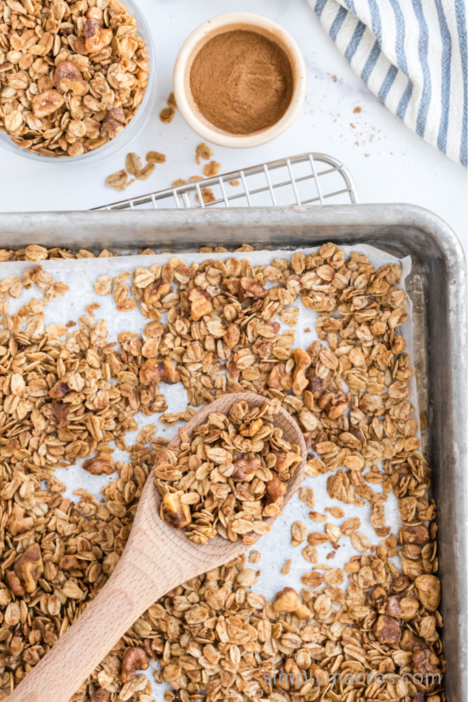 Wooden spoon on a baking sheet scooping up the baked cinnamon vanilla flavored granola. 