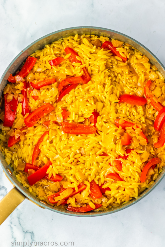 Bell pepper, onion, garlic, seasonings, and orzo mixed together in a skillet.