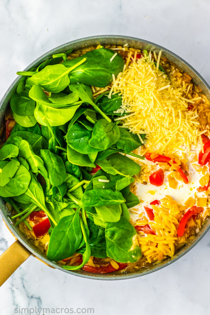 Spinach, heavy cream, and parmesan cheese added to the vegetables and orzo in a skillet.