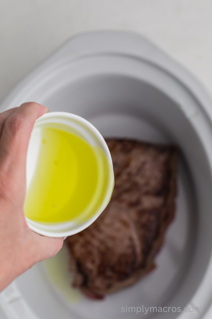 Pepperoncini juice being poured over the roast in a slow cooker.