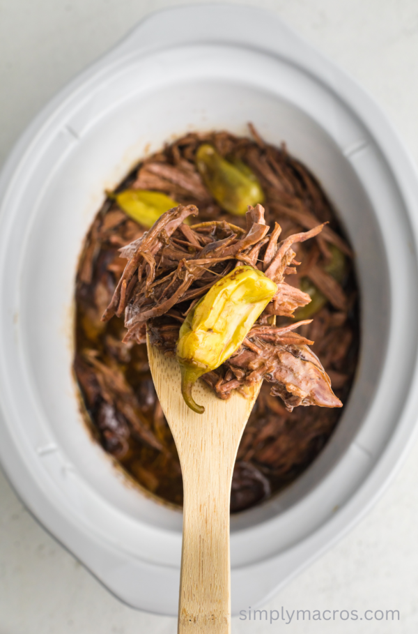 Scoop of roast with a pepperoncini pepper over a crock pot.