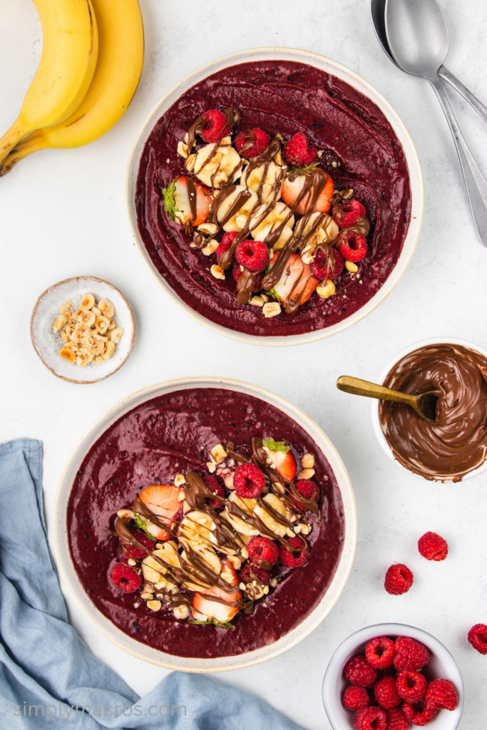 Overhead photo of two acai bowl with fruit, nuts, and drizzled with Nutella. 
