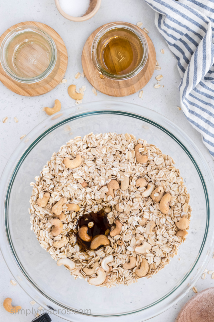 Coconut oil, agave, and vanilla extract in a bowl with oats and cashews ready to blend before baking.