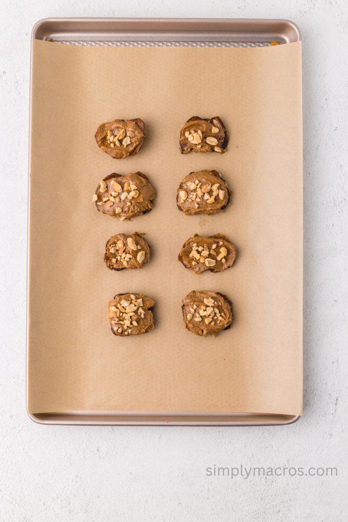 Dates topped with almond butter and peanuts on a parchment paper lined sheet. 