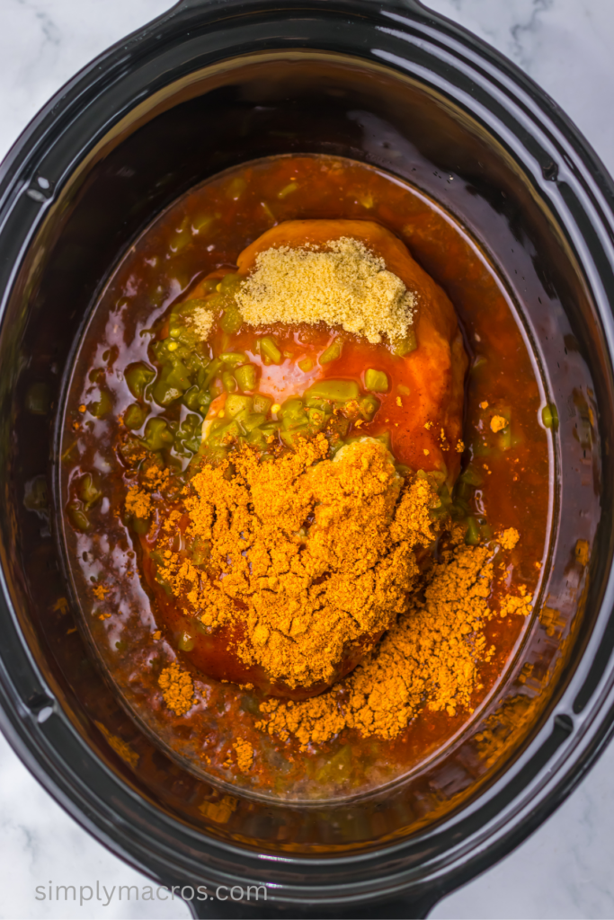 Pork in the bottom of the slow cooker topped with ingredients. 