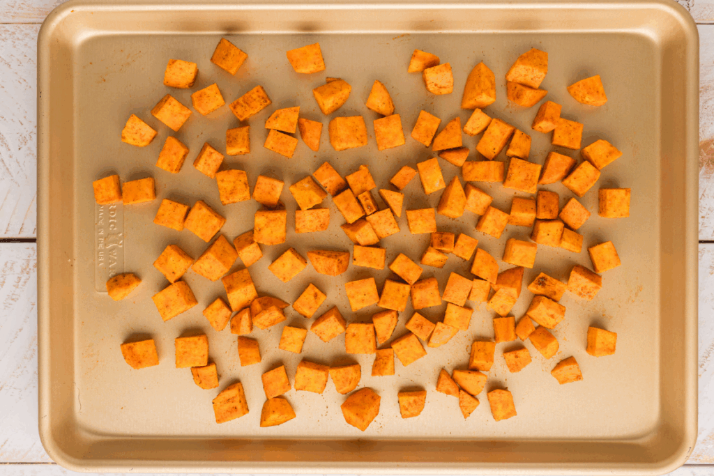 Diced and seasoned sweet potatoes on a baking sheet. 