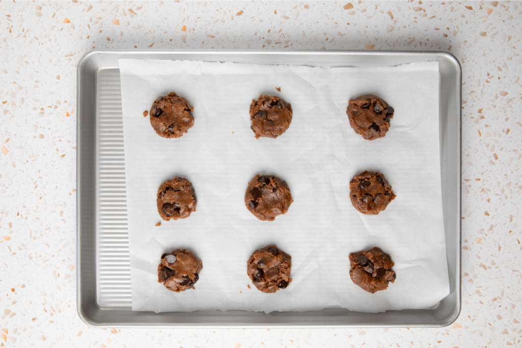 Cookie dough on a lined sheet flattened and ready to bake. 