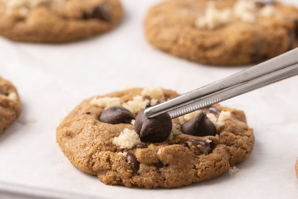Close up of almond butter cookies fresh from the oven with brown sugar and extra chocolate chips being added to the tops. 