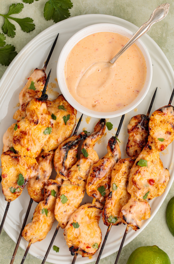 Bang bang chicken skewers on a serving tray with a bowl of sauce for serving.