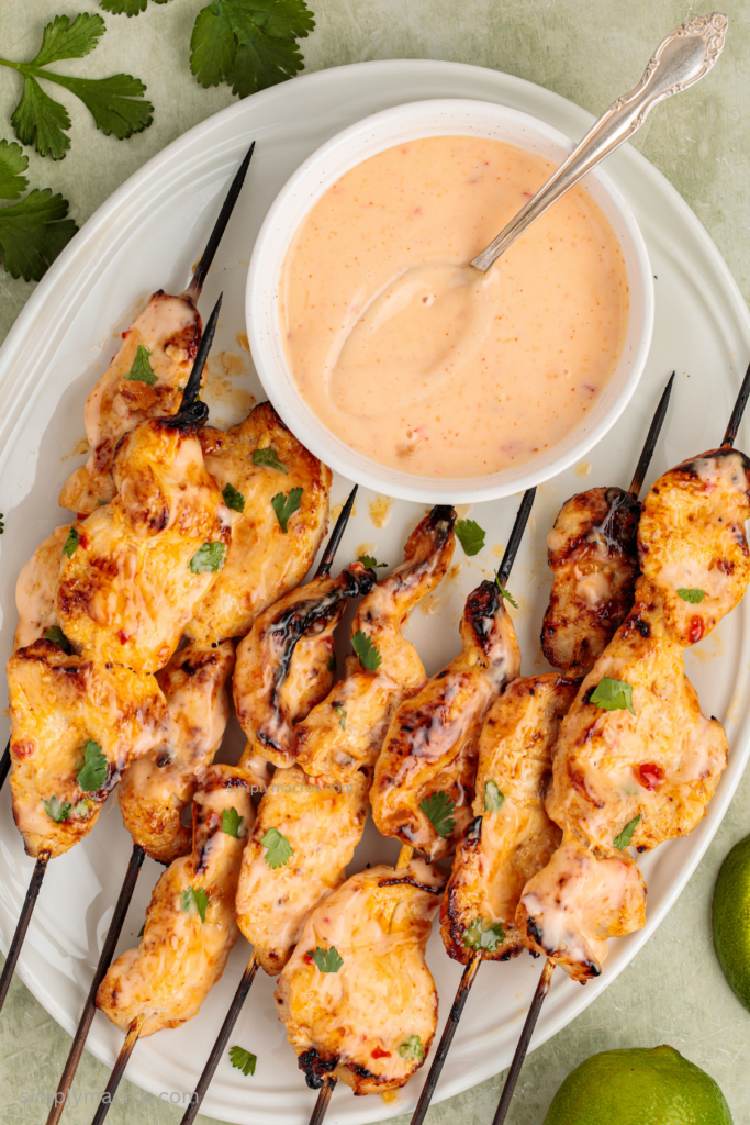 Bang bang chicken skewers on a serving tray with a bowl of bang bang sauce for dipping.