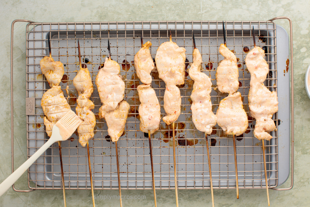 half broiled chicken skewers flipped and being brushed with additional sauce.
