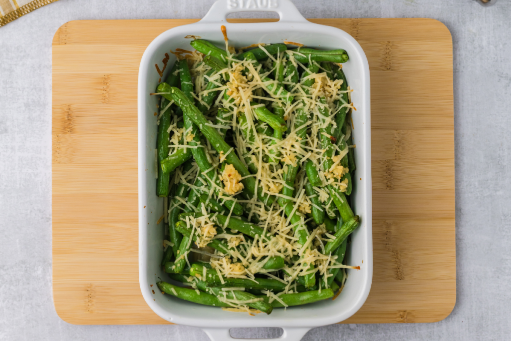 Green beans in a casserole dish topped with garlic and parmesan and seasoned with salt and pepper. 