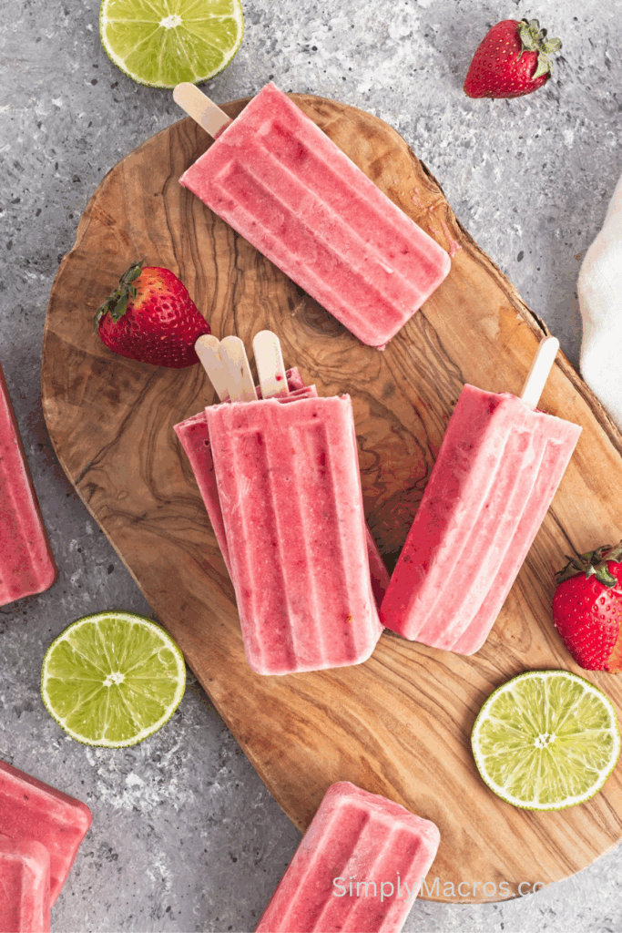 Strawberry lime coconut popsicles on a cutting board.